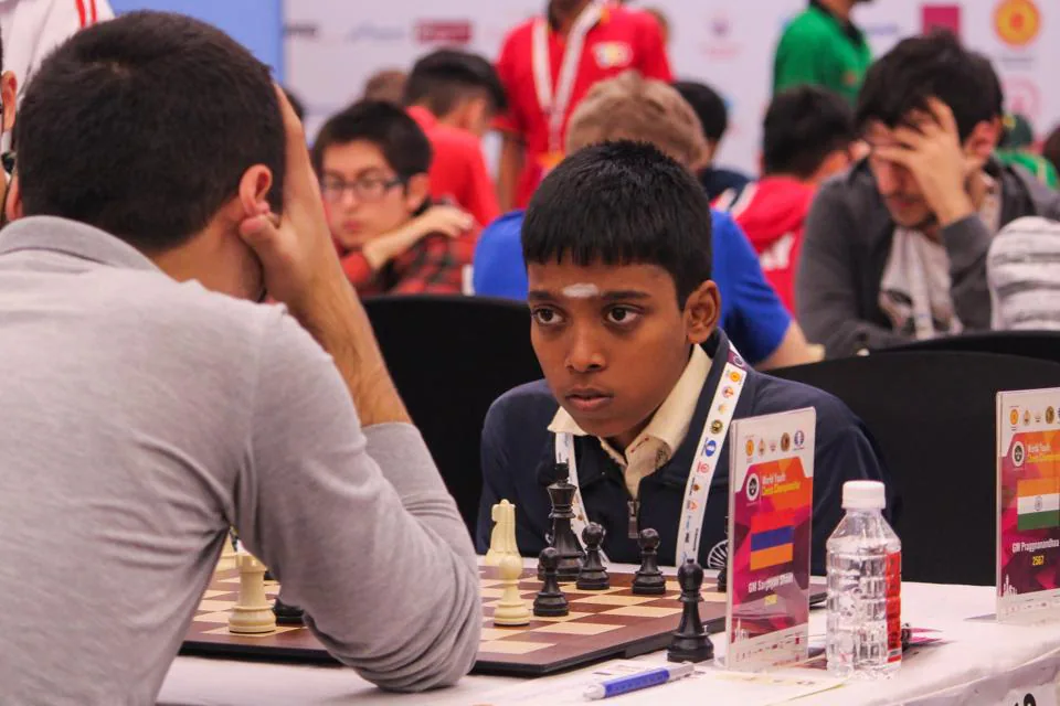 Praggnanandhaa Rameshbabu playing chess at the World Youth U18 Championship with a chessboard and a player sitting in front of him.
